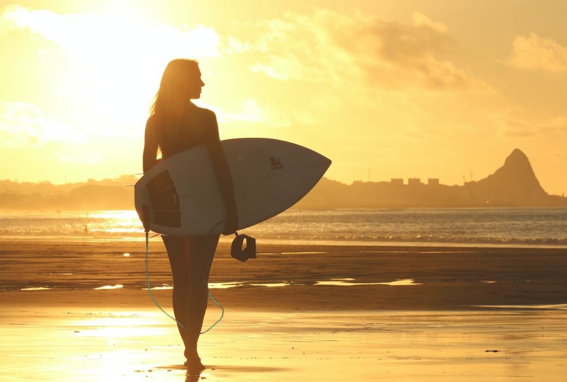 Surferin beim Sonnenuntergang am Meer - ein lebendiges Bild, das die 'Top 5 Produkte für Wellenreiter' aus den Geschenkideen für Surf-Begeisterte einfäng