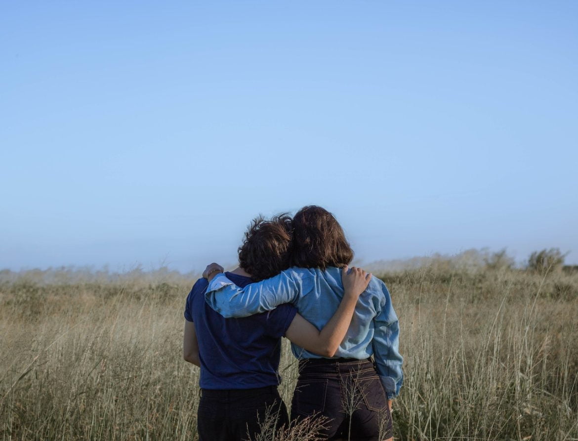 Zwei Freunde sitzen auf einer Wiese, legen die Arme um die Schultern und lehnen die Köpfe aneinander, symbolisierend die tiefe Freundschaft und Verbundenheit, die im Blogpost über Freundschaftsgeschenk: 5 einzigartige Produkte thematisiert wird