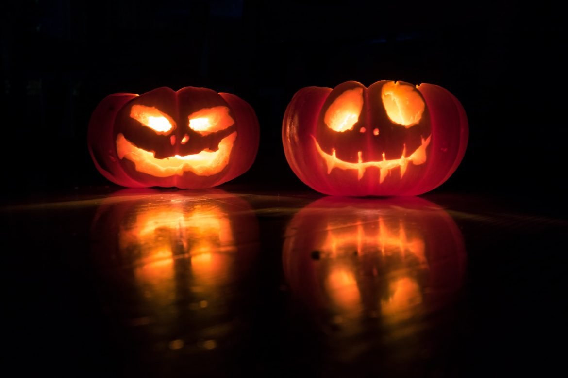Zwei orange leuchtende Kürbisse, die für Halloween dekoriert und geschnitzt wurden und Inspiration für Halloween-Geschenkideen wie Kürbisschnitzsets, Halloween-Körbe, Halloween-Geschirr und Halloween-Partyspiele liefern